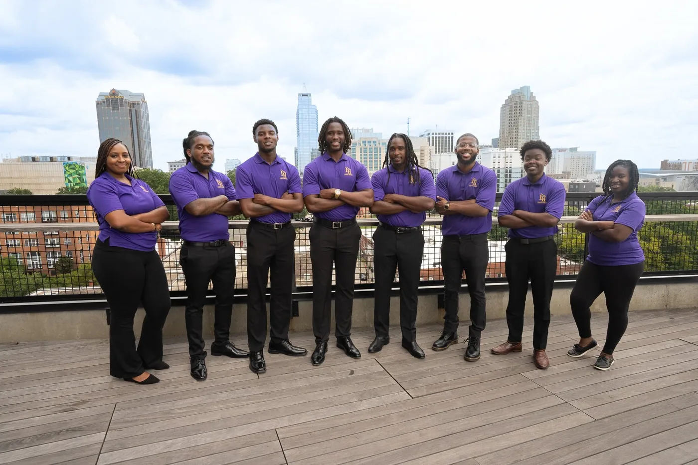 The Lamar Homes Roofing & Construction team in purple polos on a rooftop terrace with the downtown Raleigh skyline behind them